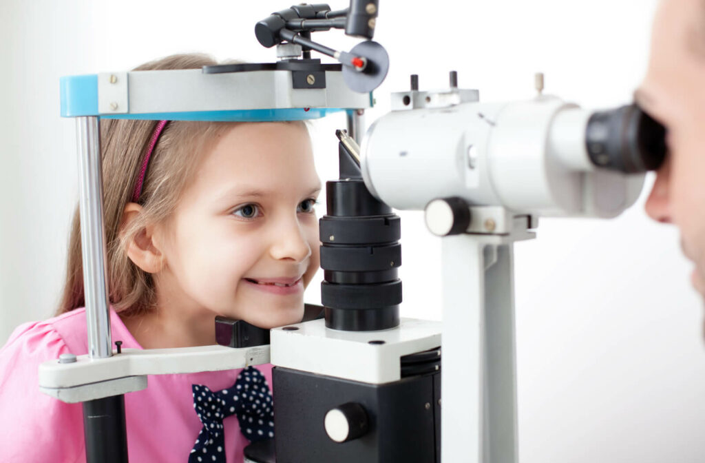A female child sitting in an optometrist's office looking into a machine that tests her vision.