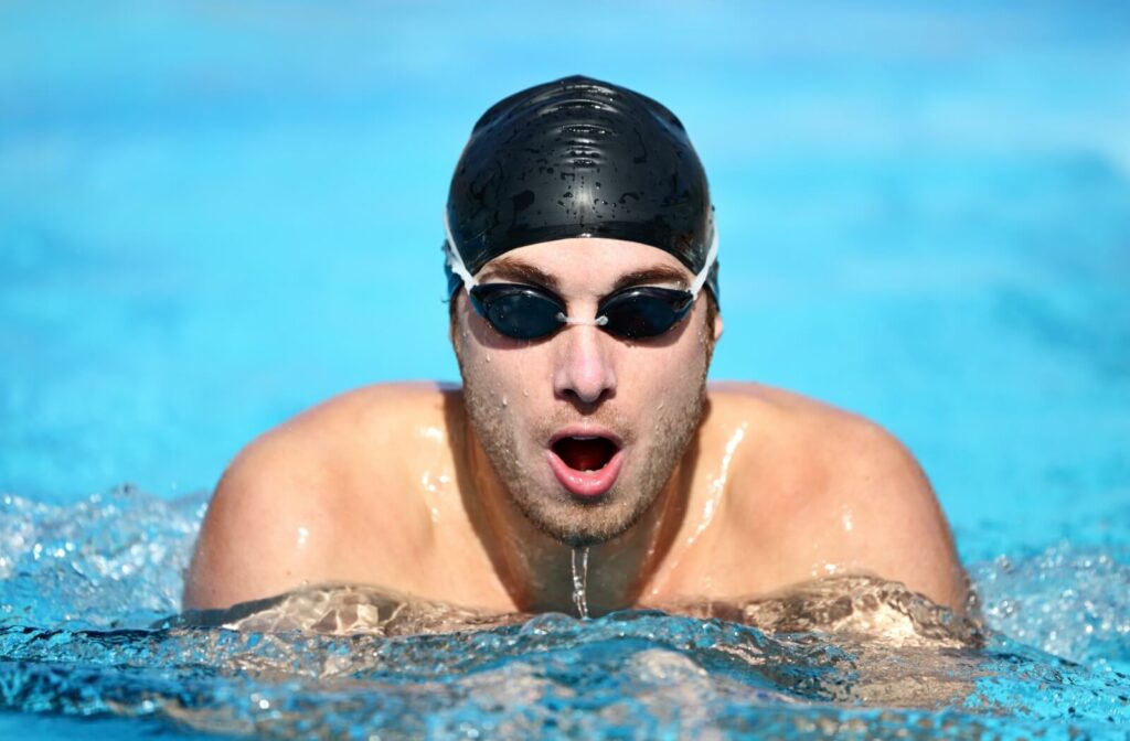 A swimmer swimming in an outdoor pool with complete swimming gear including swimming goggles.