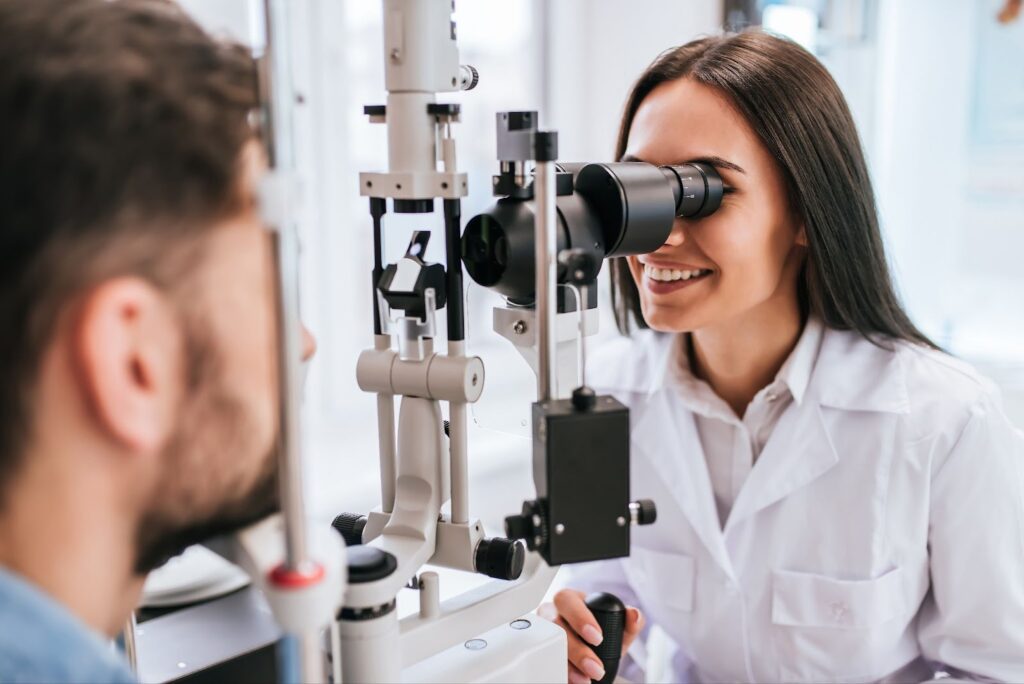 A smiling female optometrist examines a male patient's eyes in an optometry office.