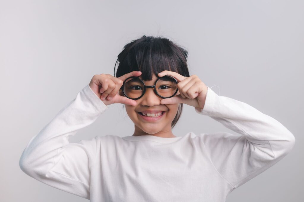 A closeup of a young child smiling while wearing her eyeglasses.