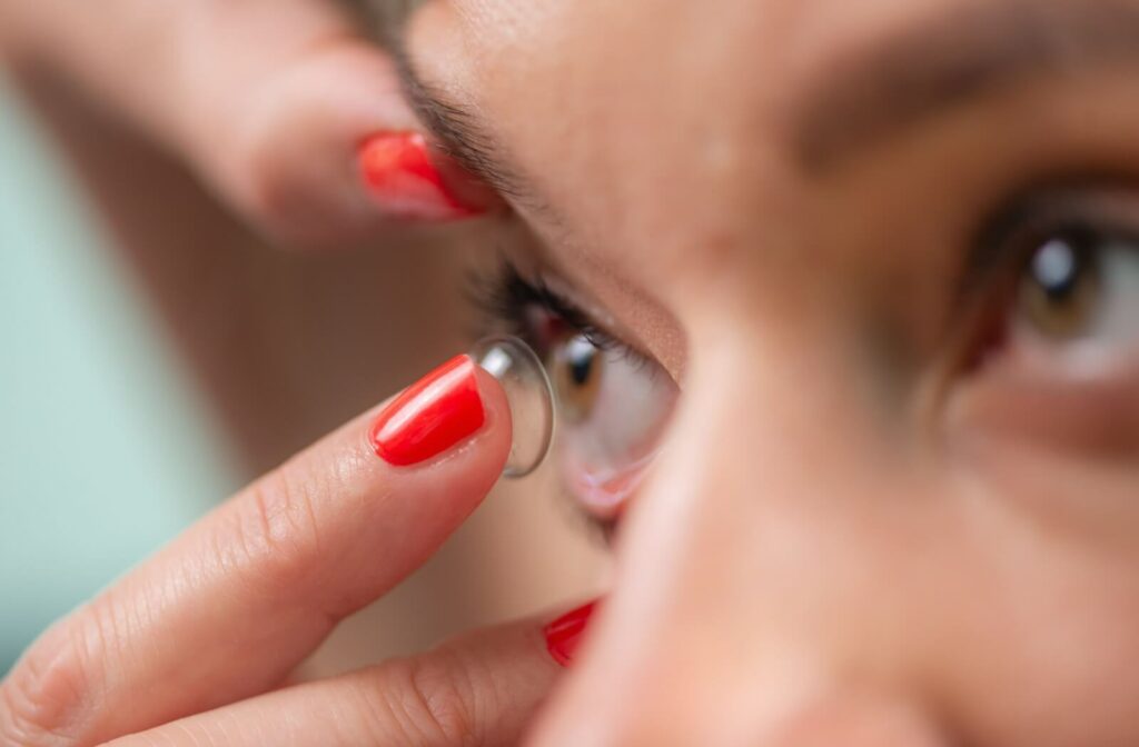 a woman is placing a fitted contact lens in her eye.