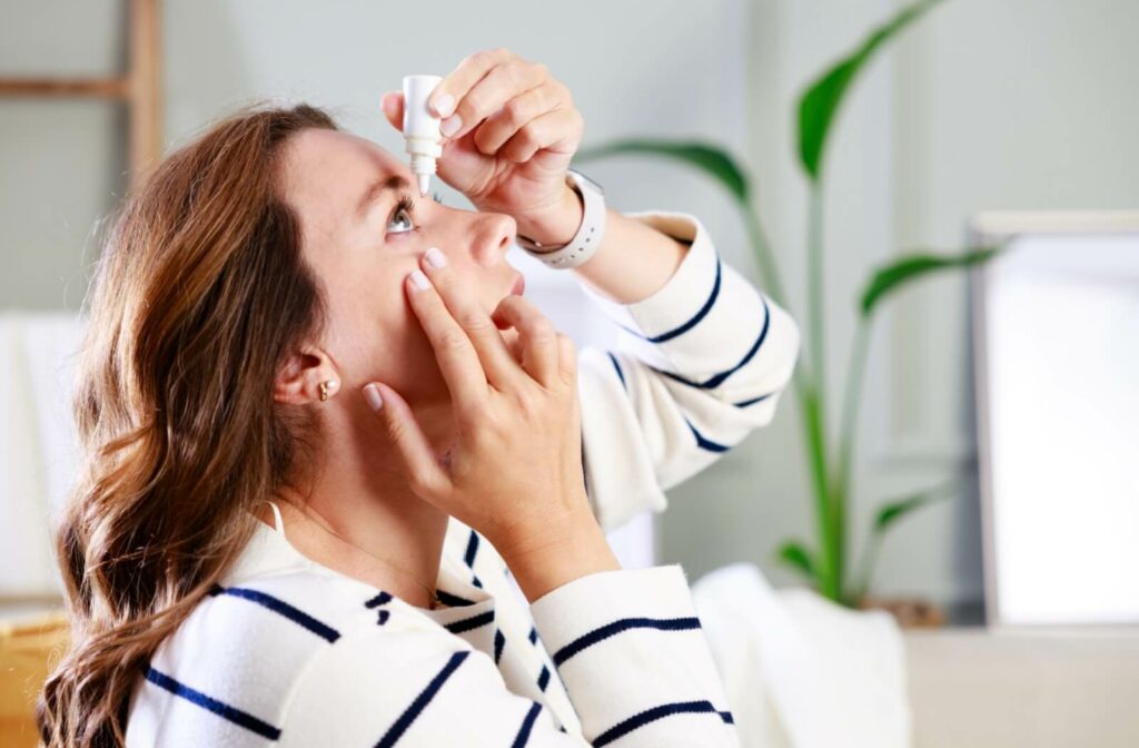 A young adult at home carefully putting eye drops in their right eye to prevent complications from dry eye.
