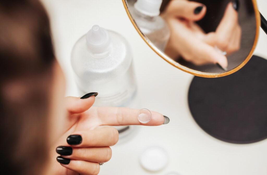 A person examining their contact lens placed on their index finger, ready to clean the lens properly with solution in the foreground
