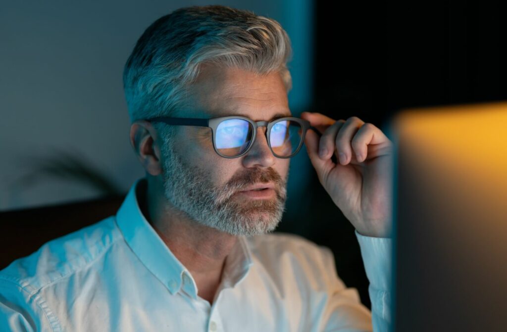 A man wearing blue light glasses while using a computer at night to reduce digital eye strain.
