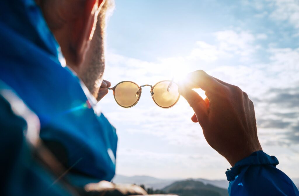 Man holding polarized sunglasses up to the sun with mountains in the background.