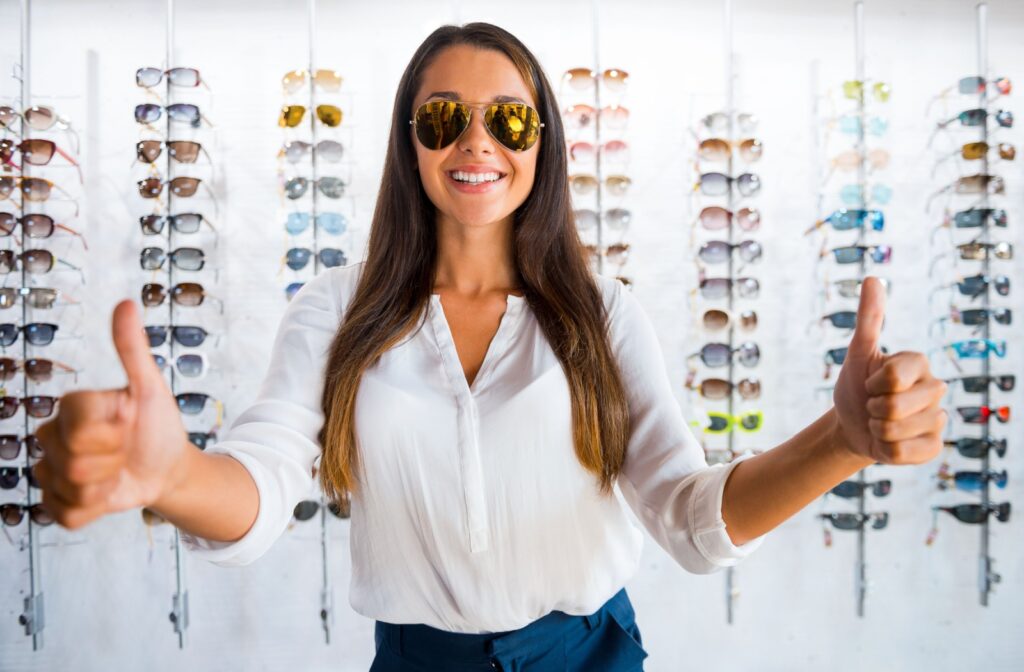 Woman wearing sunglasses giving two thumbs up in an optical store.