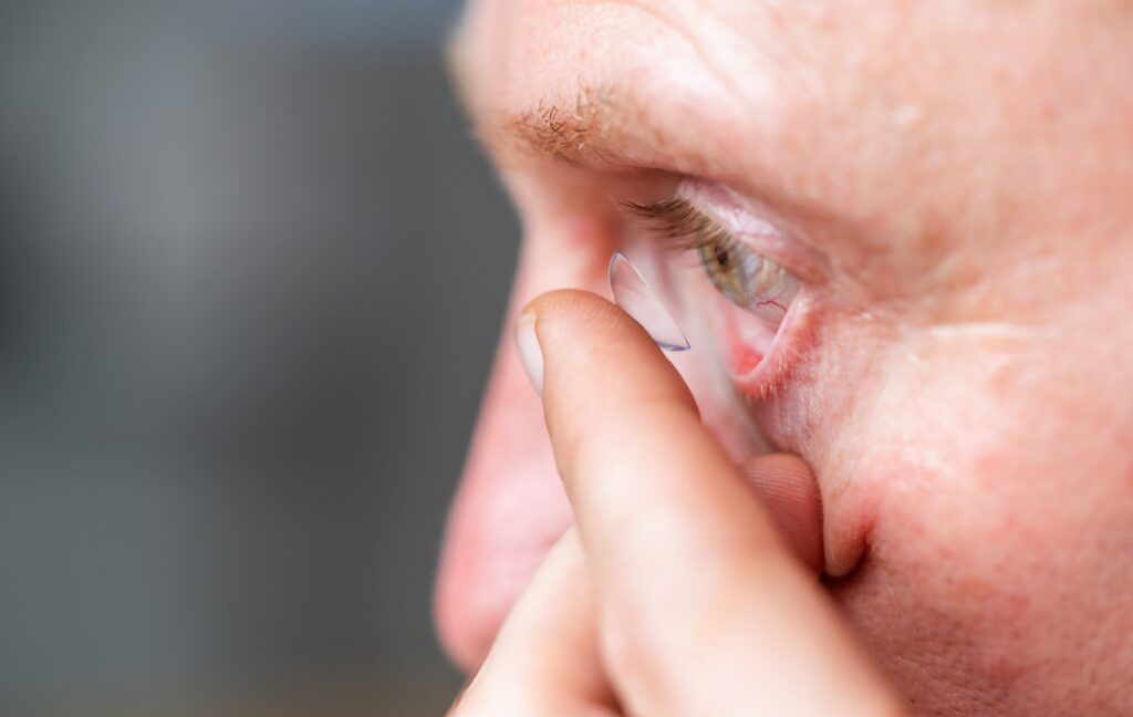 A person uses their finger to place a soft contact lens into their eye gently while staring straight ahead.