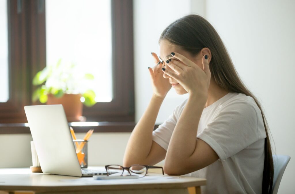 A person sitting at a computer and rubbing their dry eyes that are irritated