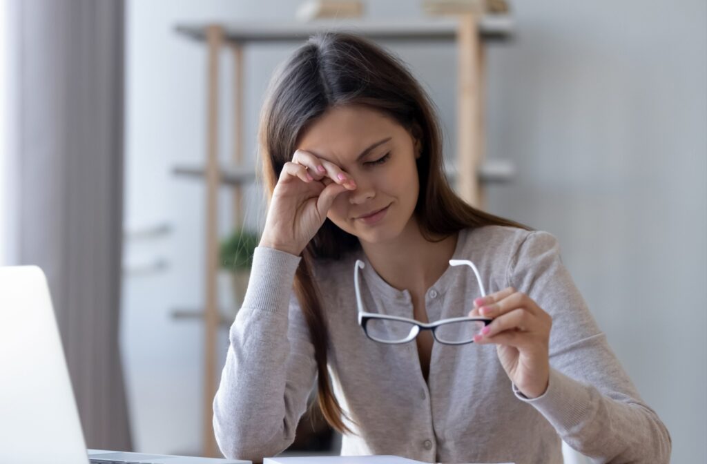 A woman holding her glasses away from her face while she rubs her eye using the back of her hand.