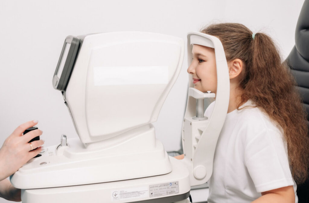A child sitting at an eye exam machine while an eye care professional adjusts the controls during a vision test.
