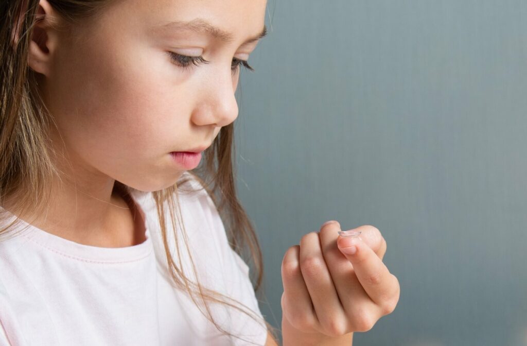 Child holding a contact lens on their fingertip and looking at it closely, preparing to put it in their eye.