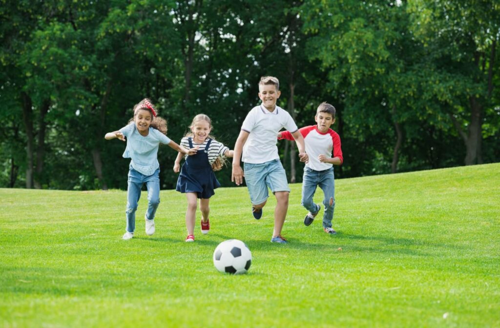 Group of children running on a grassy field while chasing a soccer ball on a sunny day.