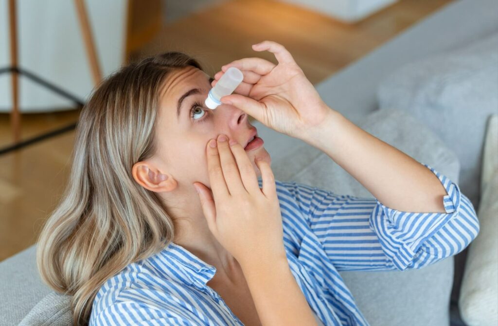 Person reclining on a couch and applying eye drops while looking upward, suggesting relief for irritated or dry eyes.