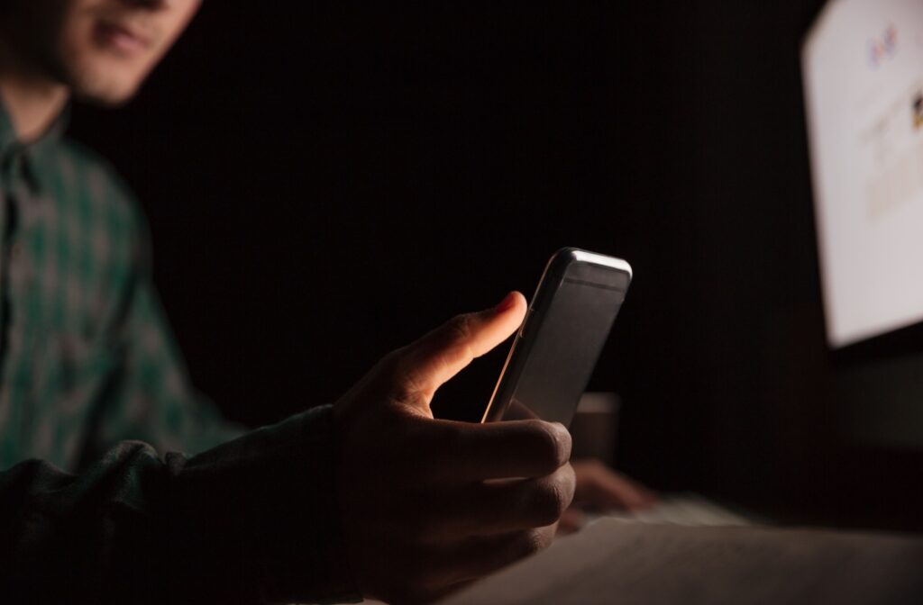 A person using their phone and computer in a dark room