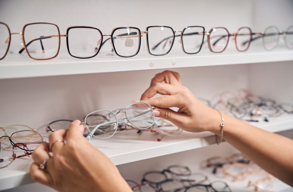 A person holding a pair of thin framed glasses amongst various pairs of other glasses.