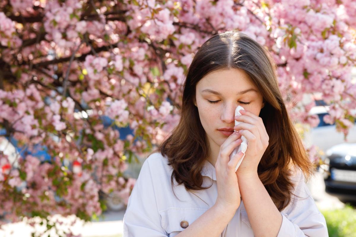 A person dabbing their eye with a tissue while standing in front of a blossoming tree.